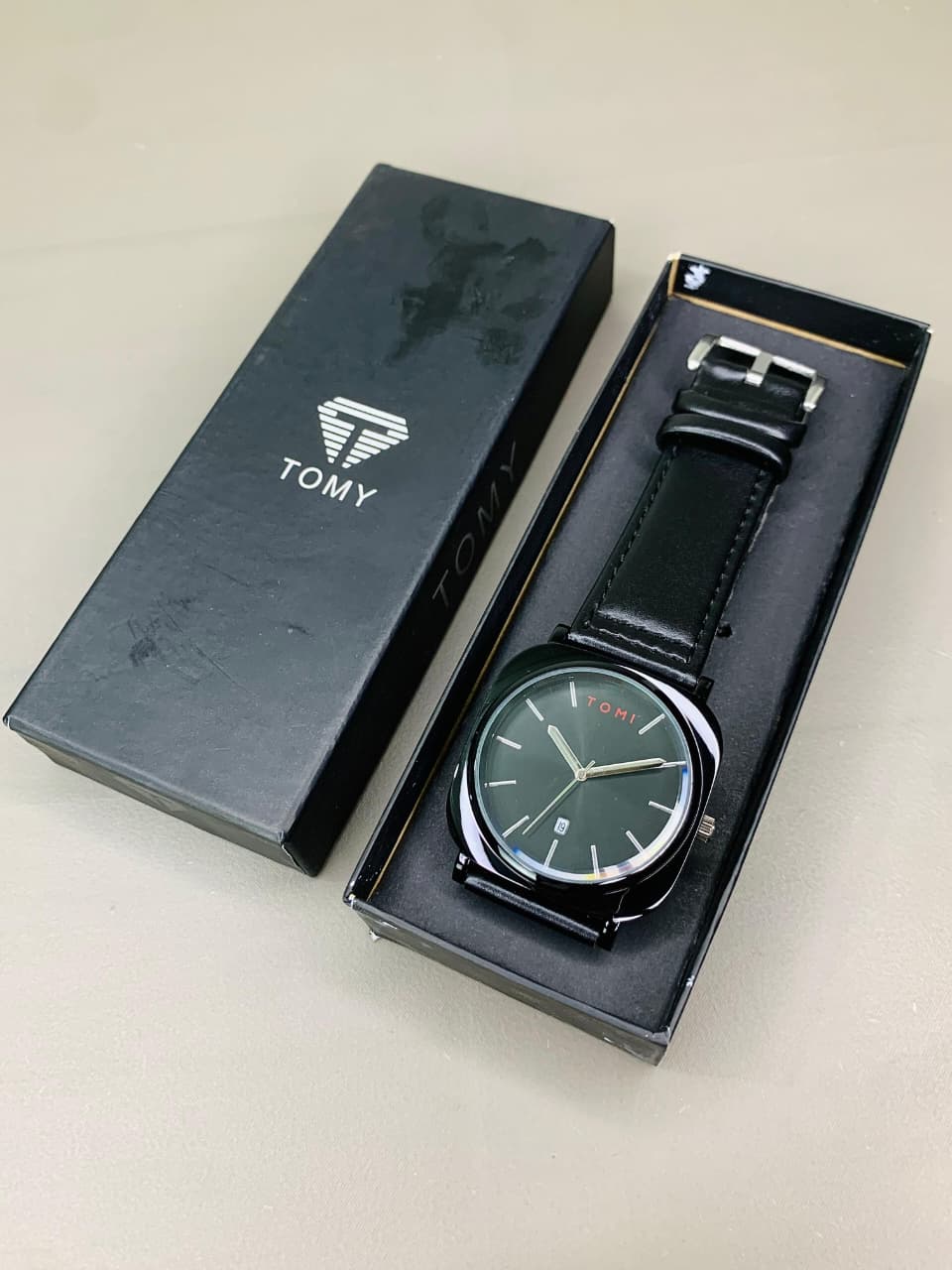 Tomy men's black leather analog watch displayed inside its premium gift box packaging.
